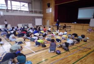 警察官が小学校で防災について小学生に説明している写真です。