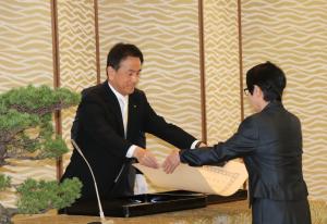 勲記と勲章を伝達する村岡知事の写真
